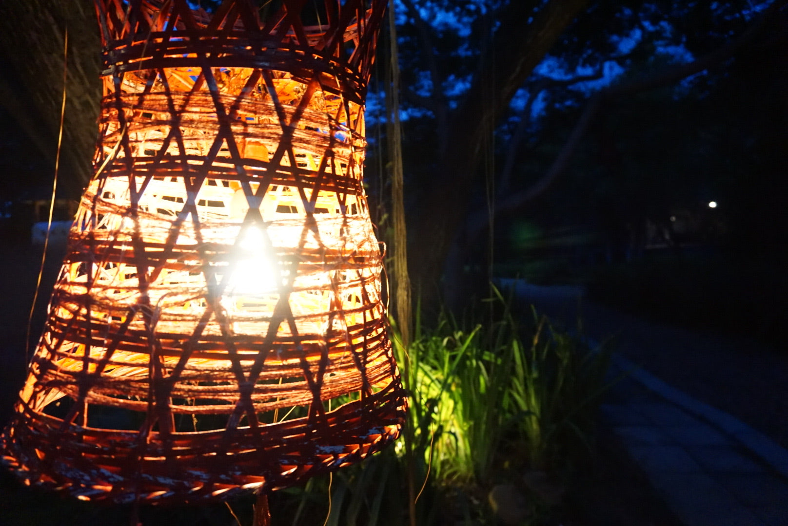 Wicker lantern emitting a warm glow in a dark outdoor setting